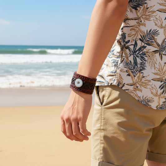 A close-up of a person's wrist wearing a wide brown leather cuff bracelet with a braided pattern and a round silver-tone button closure, paired with a navy polka-dot shirt and light beige pants.