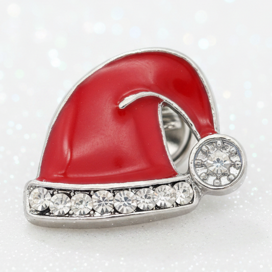 A Santa hat snap button featuring a glossy red enamel body, a silver-tone metal base, and a row of clear rhinestones along the brim, with a small round clear stone on the side. The brooch is photographed on a white background with subtle sparkling bokeh.